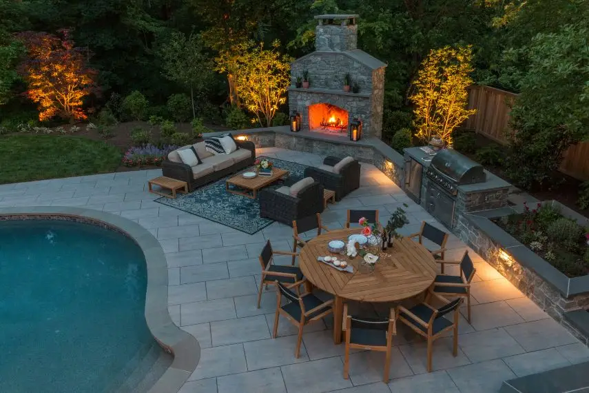 Landscape lighting adds warmth to trees surrounding an outdoor fireplace in Alexandria Virginia